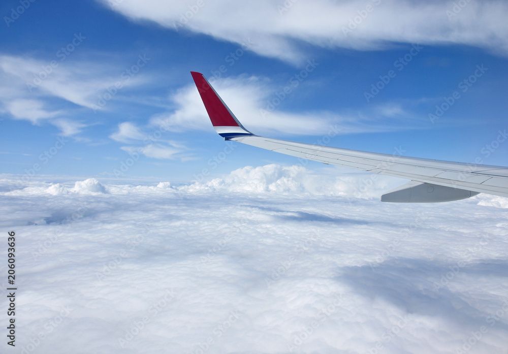 The wing of a transport plane flying over white clouds with a blue sky. The wing of a transport plane flying over white clouds with a blue sky.