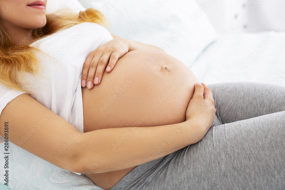 Happy pregnancy. Close up of female hands caressing tummy while posing on light background Happy pregnancy. Close up of female hands caressing tummy while posing on light background