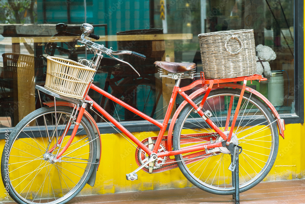 Red vintage bicycle with rattan baskets parked near yellow wall container style coffee shop.