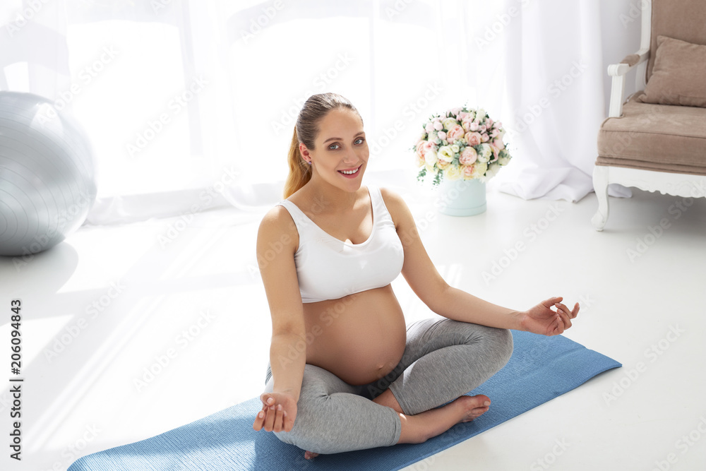 Life balance. Jovial pregnant woman sitting on mat board and staring at camera Life balance. Jovial pregnant woman sitting on mat board and staring at camera
