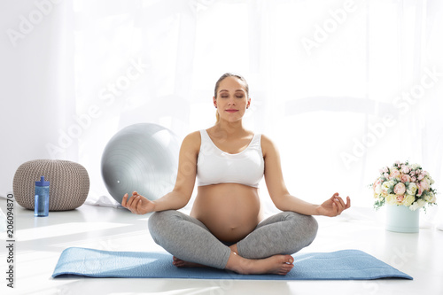 Calm mind. Focused pregnant woman sitting on mat board and closing eyes