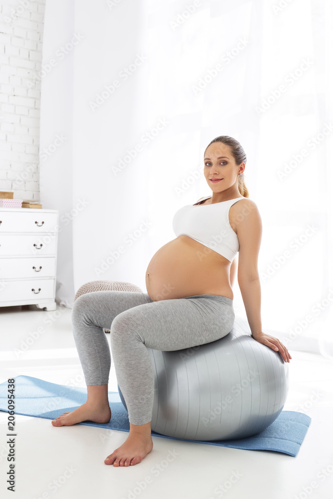 Physical poses. Happy pregnant woman sitting on gym ball and looking at camera Physical poses. Happy pregnant woman sitting on gym ball and looking at camera