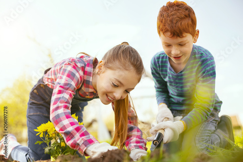 Pleasurable time. Delighted positive children having fun while working in the garden together