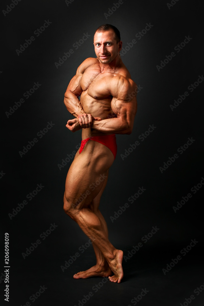 Foto Stock Studio shot of young male bodybuilder posing, showing side  biceps and chest pose, on black background. | Adobe Stock