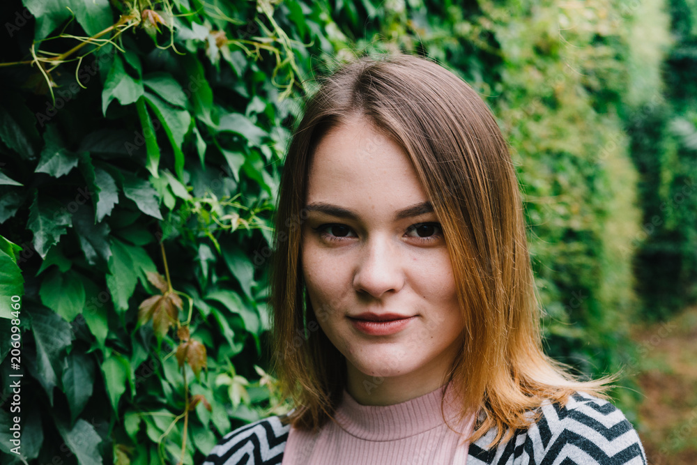 Portrait of a stylish woman against a green foliage background.