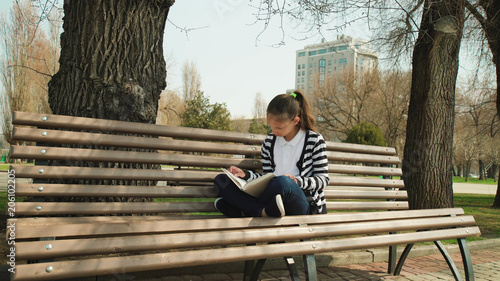 outdoor park education. leisure time. Young cute teen sitting bench reading book.