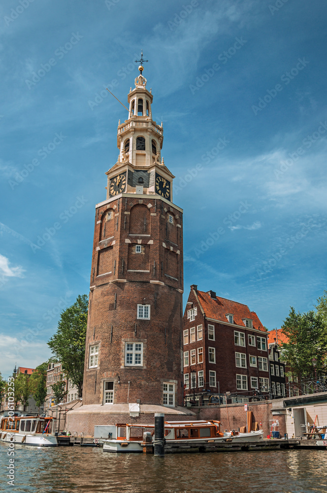 Old brick bell tower and bridge near the tree-lined canal with moored boats and blue sky in Amsterdam. Famous for its huge cultural activity, graceful canals and bridges. Northern Netherlands. Old brick bell tower and bridge near the tree-lined canal with moored boats and blue sky in Amsterdam. Famous for its huge cultural activity, graceful canals and bridges. Northern Netherlands.