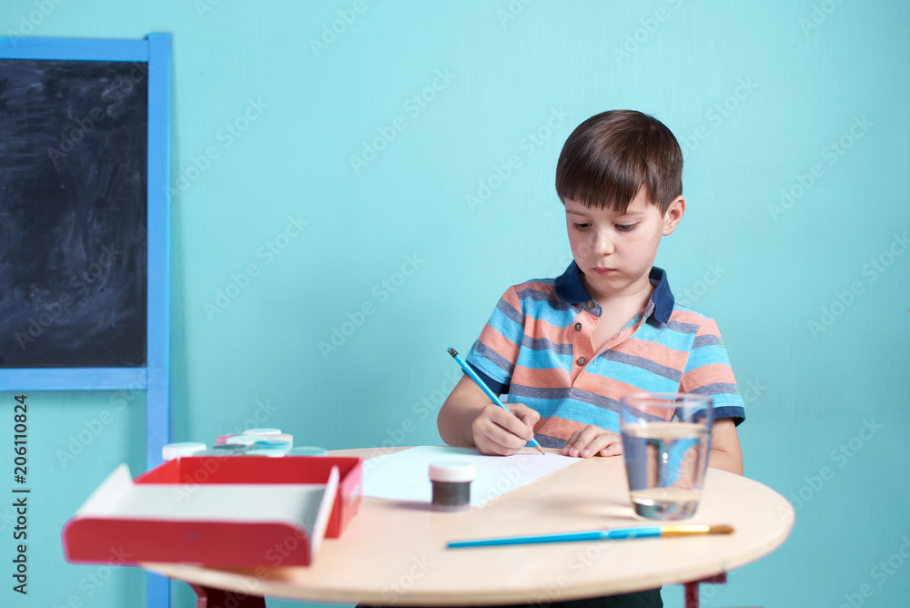 Caucasian boy carefully doing a sketch with pencil before painting with watercolors. Caucasian boy carefully doing a sketch with pencil before painting with watercolors.