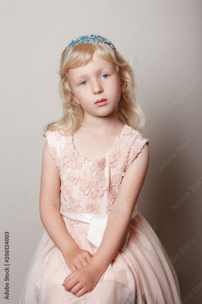 Closeup portrait of cute adorable white blonde fair Caucasian preschool girl in pink dress and princess crown. Pensive sad hild posing in studio on plain light background. Closeup portrait of cute adorable white blonde fair Caucasian preschool girl in pink dress and princess crown. Pensive sad hild posing in studio on plain light background.