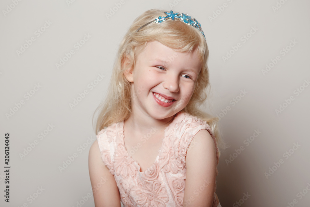 Closeup portrait of cute adorable white blonde fair Caucasian preschool girl in pink dress and princess crown. Child smiling laughing posing in studio on plain light background. Closeup portrait of cute adorable white blonde fair Caucasian preschool girl in pink dress and princess crown. Child smiling laughing posing in studio on plain light background.