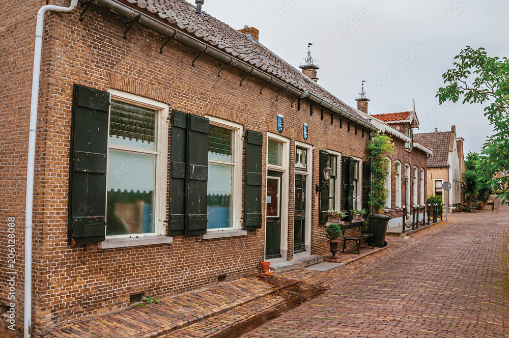 Charming and quiet alley with brick rustic houses and greenery in cloudy day at Drimmelen. A lovely small hamlet with harbor and elegance streets. Southern Netherlands.