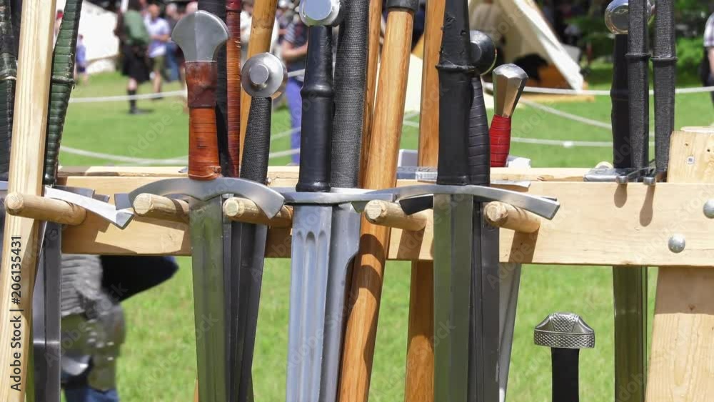 medival swords and weaponry on rack panning as knight walks by in background 4k medival swords and weaponry on rack panning as knight walks by in background 4k