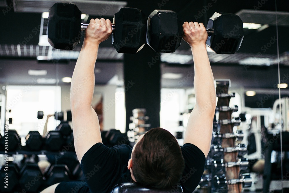 Muscular man lifts black weights up while lying in gym Muscular man lifts black weights up while lying in gym