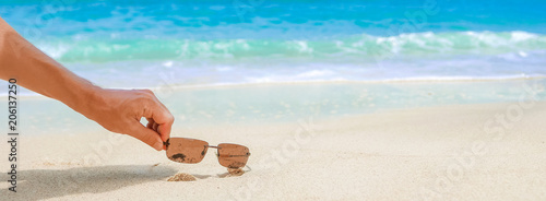 Commercial background, hand picking up the product from sandy beach on blue ocean background