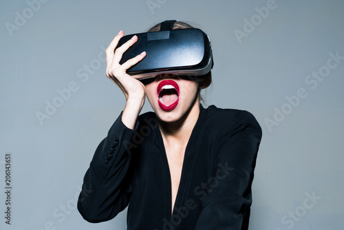 Surprised woman using VR headset. Emotional girl in virtual reality goggles. Connection, technology progress concept. Virtual reality glasses, entertainment. Woman with red lips adjust virtual reality