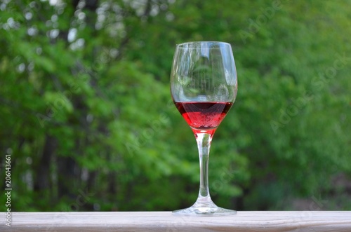 Wine glass and red wine on the wood railing with a green tree background