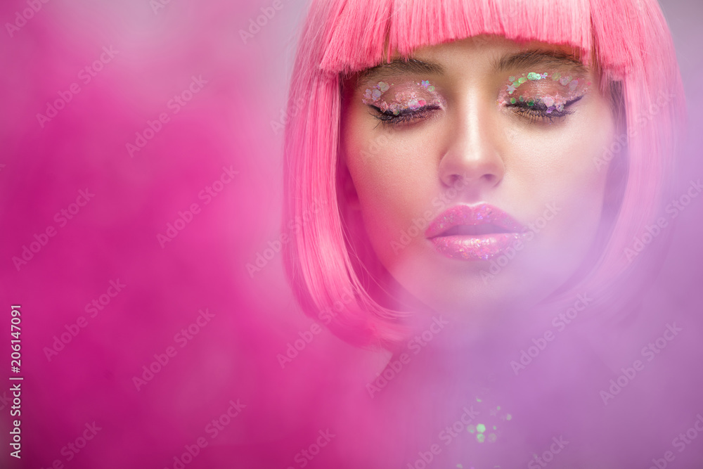 attractive woman with pink hair and makeup with glitter standing in pink smoke with closed eyes