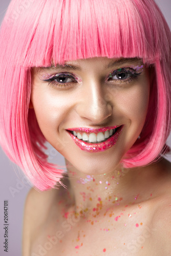 smiling attractive woman with pink hair and makeup with glitter looking at camera isolated on violet
