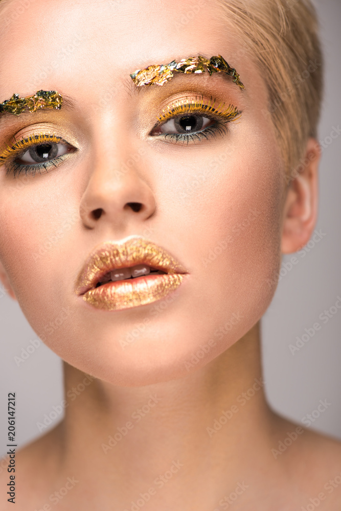 attractive stylish woman with golden glitter on face looking at camera isolated on grey
