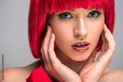 attractive woman with red hair and glittering makeup touching face isolated on grey