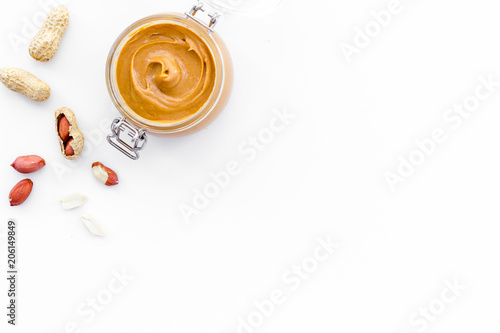Peanut butter in glass jar near peanut on white background top view copy space