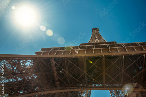 Bottom view of Eiffel Tower made in iron, with sunny blue sky in Paris. Known as the “City of Light”, is one of the most impressive world’s cultural center. Northern France. Retouched photo