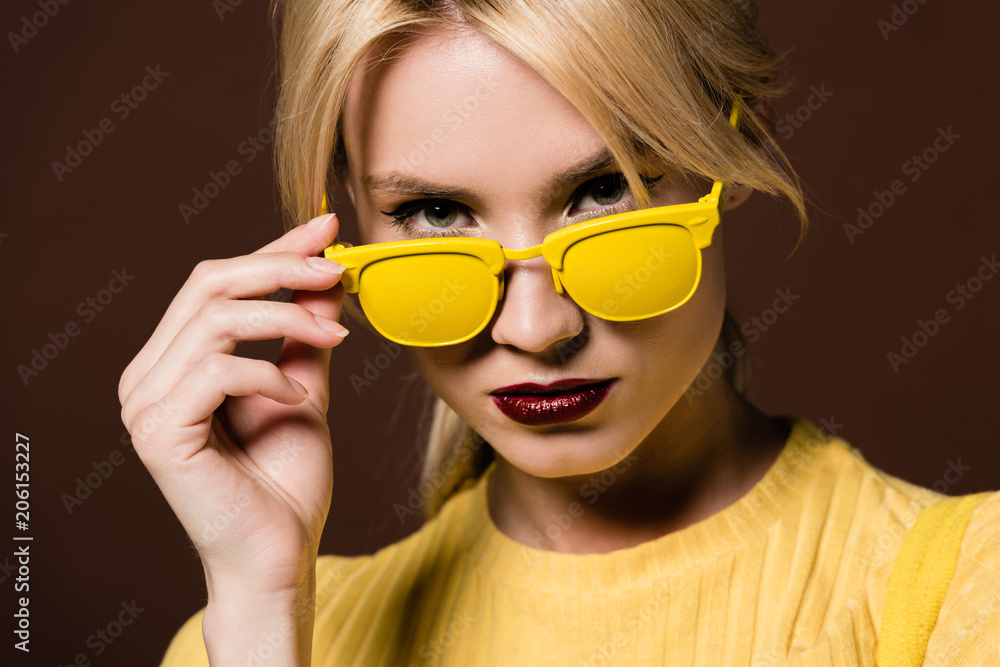 close-up portrait of beautiful young blonde woman in yellow sunglasses looking at camera isolated on brown close-up portrait of beautiful young blonde woman in yellow sunglasses looking at camera isolated on brown