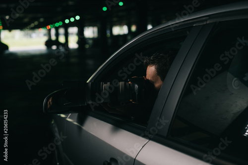 male paparazzi doing surveillance by camera with object glass from his car