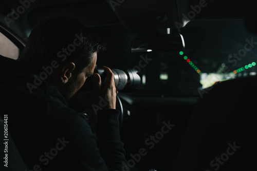 back view of focused man doing surveillance by camera with object glass from his car photo