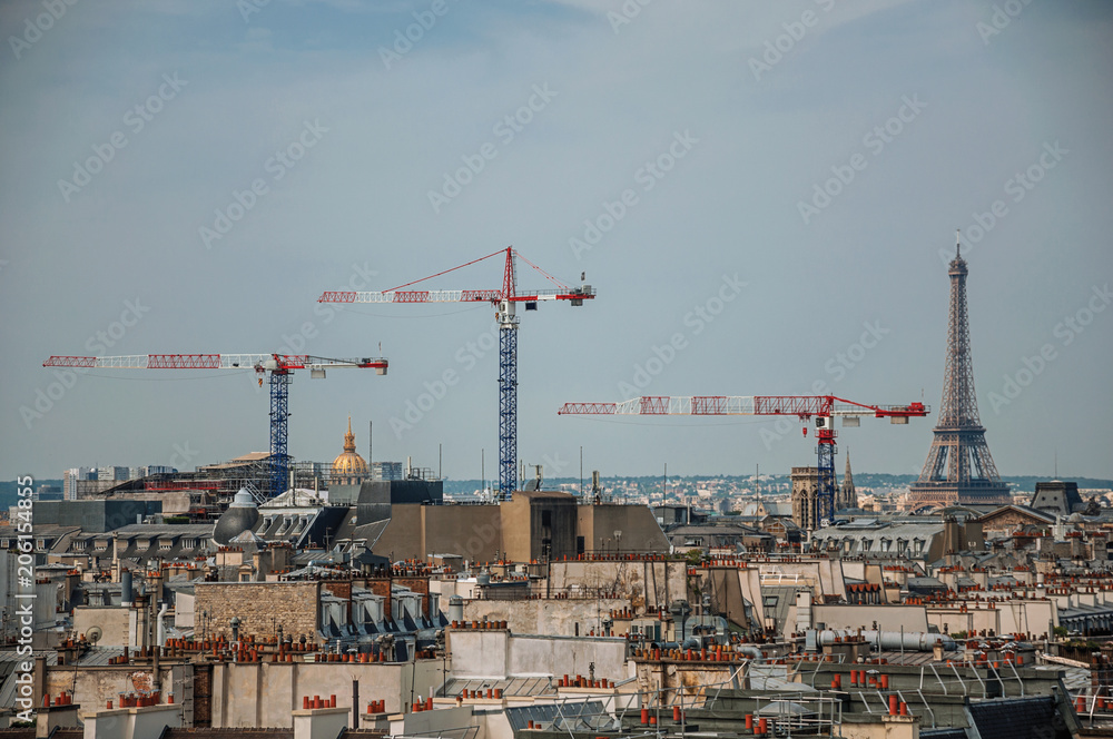 Close-up of buildings rooftops, cranes and Eiffel Tower on the horizon in Paris. Known as the “City of Light”, is one of the most impressive world’s cultural center. Northern France. 