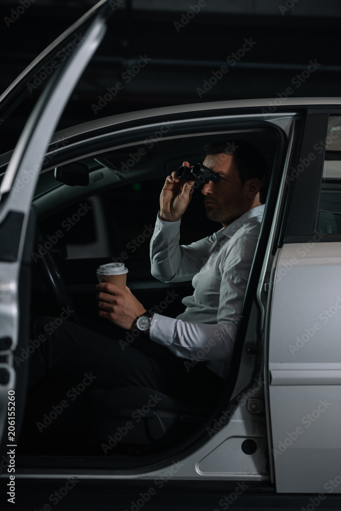 undercover male agent spying by binoculars and drinking coffee in