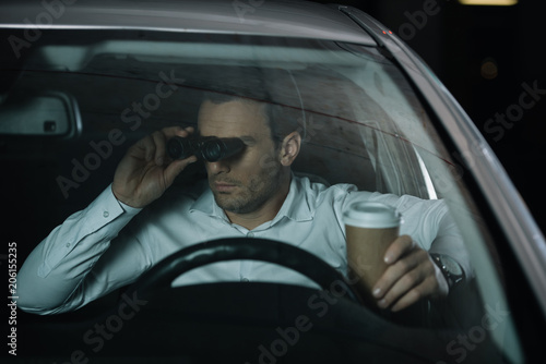 undercover male agent doing surveillance by binoculars and drinking coffee in car © LIGHTFIELD STUDIOS