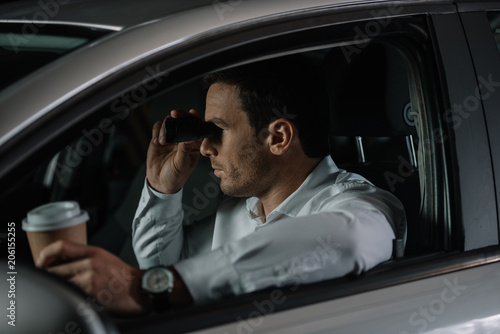side view of undercover male agent doing surveillance by binoculars and drinking coffee in car © LIGHTFIELD STUDIOS