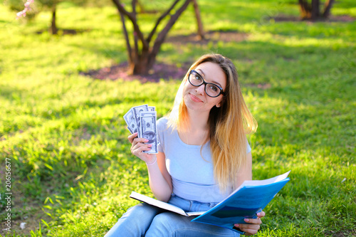 Successsful female landscape designer sitting on green grass with black folder and keeping money. Concept of earning money and studying in open air. photo