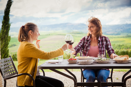 happy female friends having lunch outdoors in beautiful scenery, Tuscany, Italy