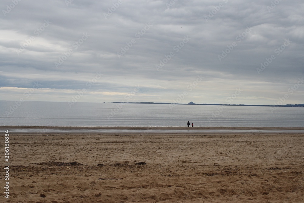 Two people walking on a beach on a cloudy day