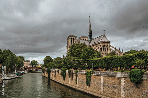 Back of the gothic Cathedral of Notre-Dame, wooded garden and Seine River with boats in Paris. Known as the “City of Light”, is one of the most impressive world’s cultural center. Northern France.