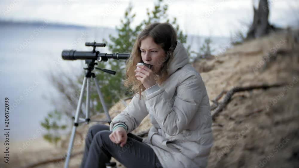 Attractive woman looks through a telescope in a forest on the river bank Attractive woman looks through a telescope in a forest on the river bank