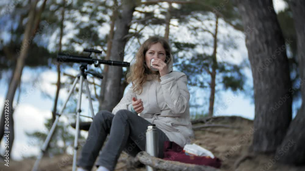 Attractive woman looks through a telescope in a forest on the river bank Attractive woman looks through a telescope in a forest on the river bank