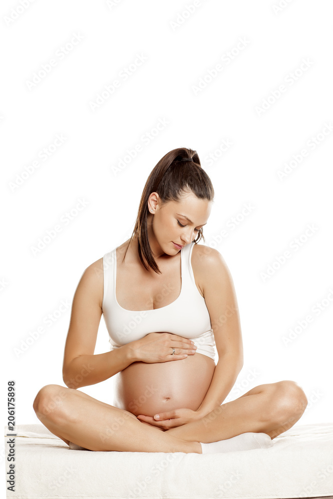 young pregnant woman sitting on a bed in the lotus position on a white background young pregnant woman sitting on a bed in the lotus position on a white background