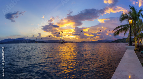 Nha Trang bay in sunset with cable car system and street lamp, branches of coconut tree on foreground photo