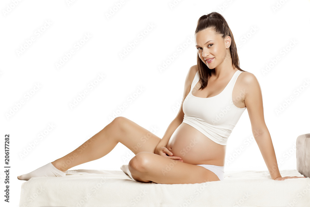young pregnant pretty woman sitting on a bed on a white background young pregnant pretty woman sitting on a bed on a white background