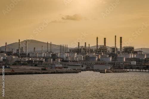 Skyline industrial area Cagliari, Sardinia Italy. View from the sea of an oil refinery plant from industry zone with cloudy sky at sunset. Oil storage tank in port area.