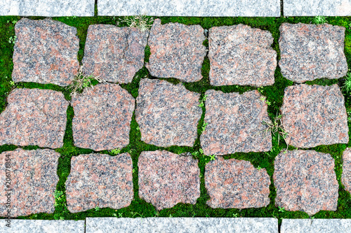 Texture, background of sett blocks different texture. Vintage, Rusty tiled, colorful, decorative granite pavement with green grass and moss.