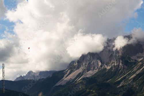 Fototapeta Naklejka Na Ścianę i Meble -  Paraglider flying over Schladming town with Dachstein mountains background, Northern Limestone Alps, Austria, dramatic cloudy sky