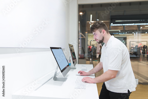 Man uses a computer in a modern electronics store. Buyer selects a monoblock in a light tech store. Buy a computer. Purchase monoblock. Choosing a computer in the store