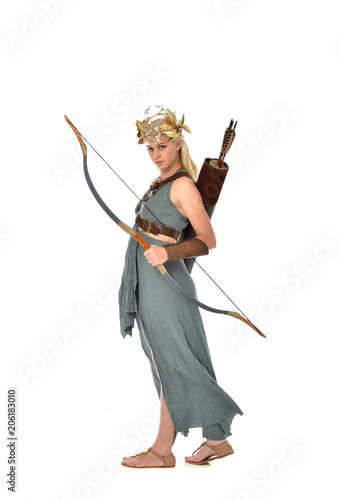 full length portrait of pretty blonde lady wearing fantasy toga gown, and holding a bow and arrow. standing pose on white background.