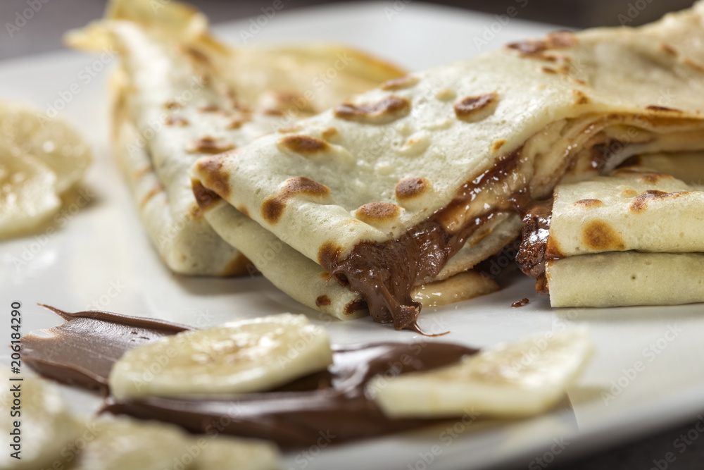 French style crepes with banana, chocolate sauce on a white plate