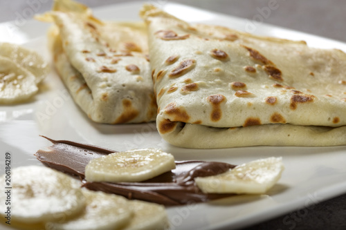 French style crepes with banana, chocolate sauce on a white plate