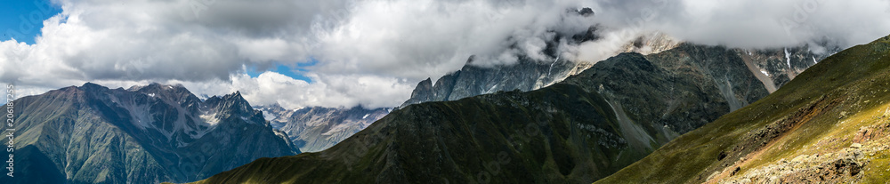 Amazing panoramic view to Caucasus Mountains. High mountain peaks in .thick and dark cumulus clouds. Sunny day in dark mountains. Svaneti, Geogria. Amazing panoramic view to Caucasus Mountains. High mountain peaks in .thick and dark cumulus clouds. Sunny day in dark mountains. Svaneti, Geogria.
